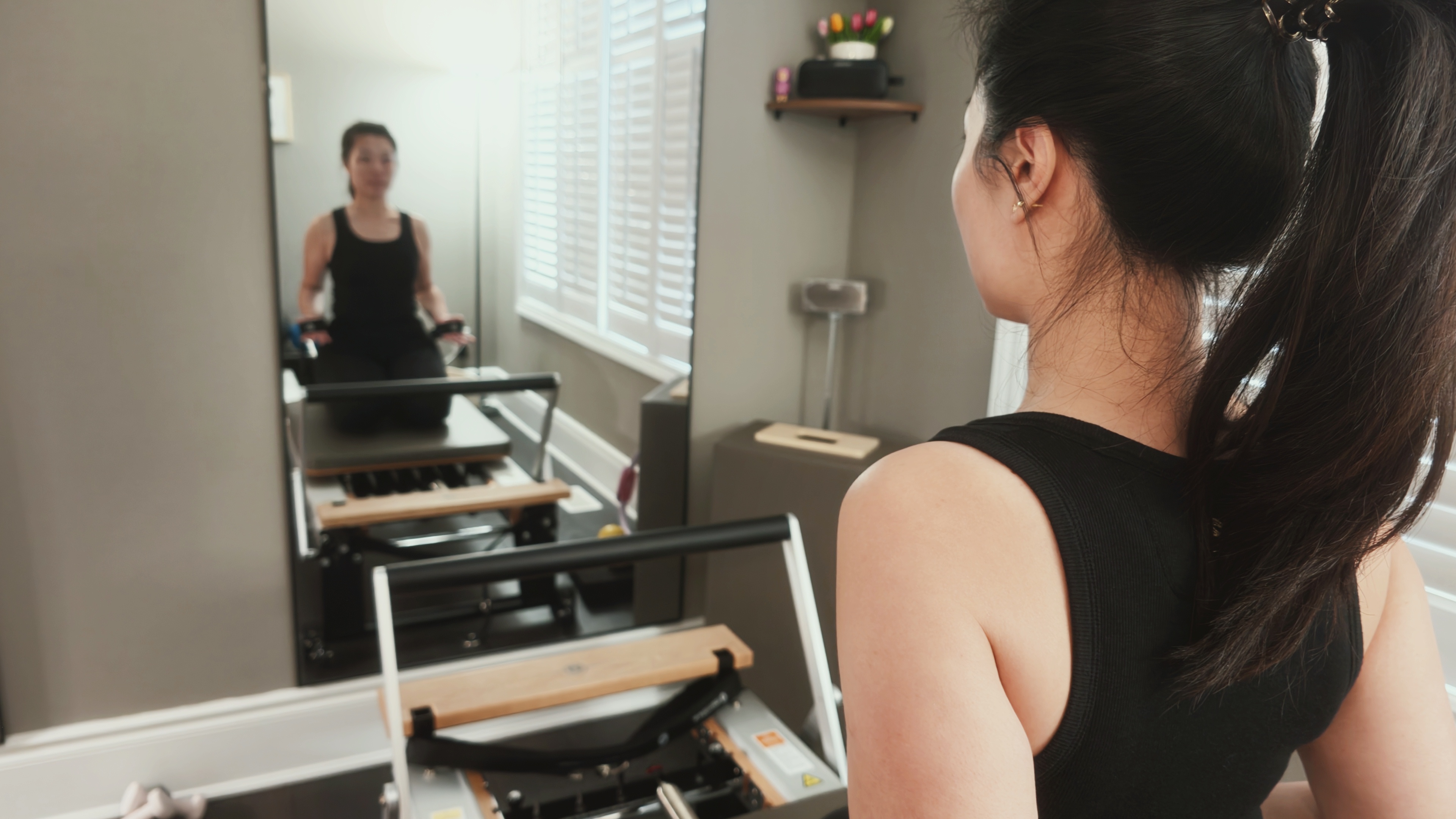Karen on the Reformer, seen over her shoulder with her reflection in the studio mirror